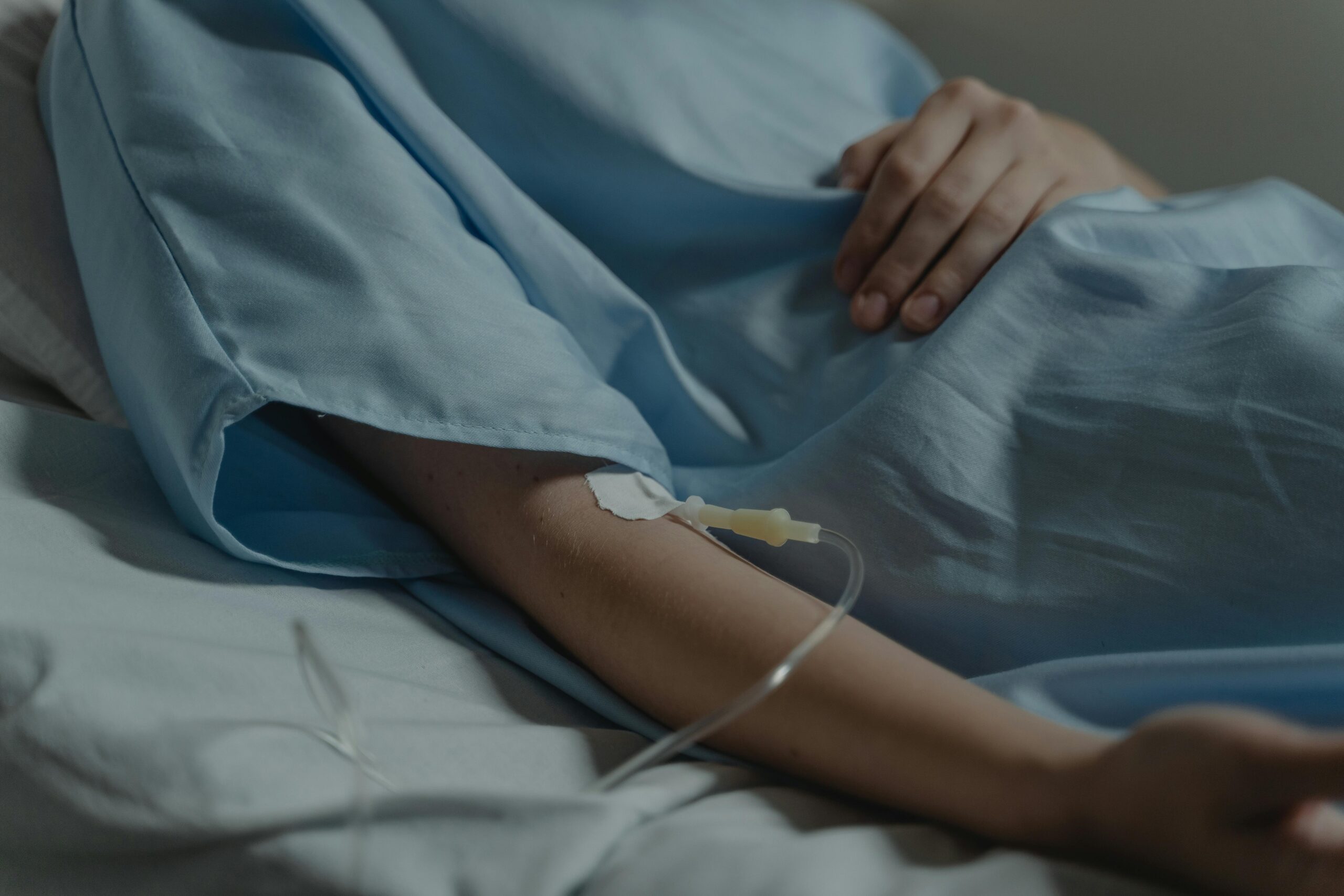 Close-up of a patient in a hospital bed with an IV drip attached to the arm.